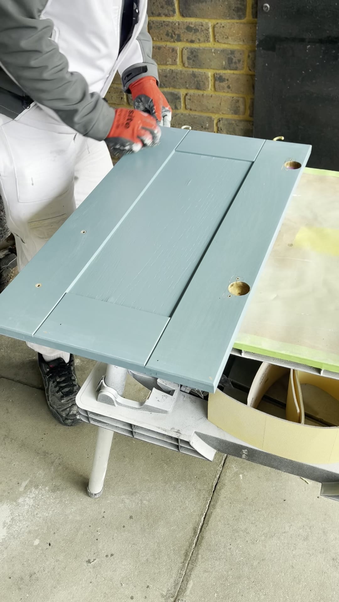 Sprayer checking a freshly sprayed blue-grey shaker kitchen door for an even, brush-mark-free finish