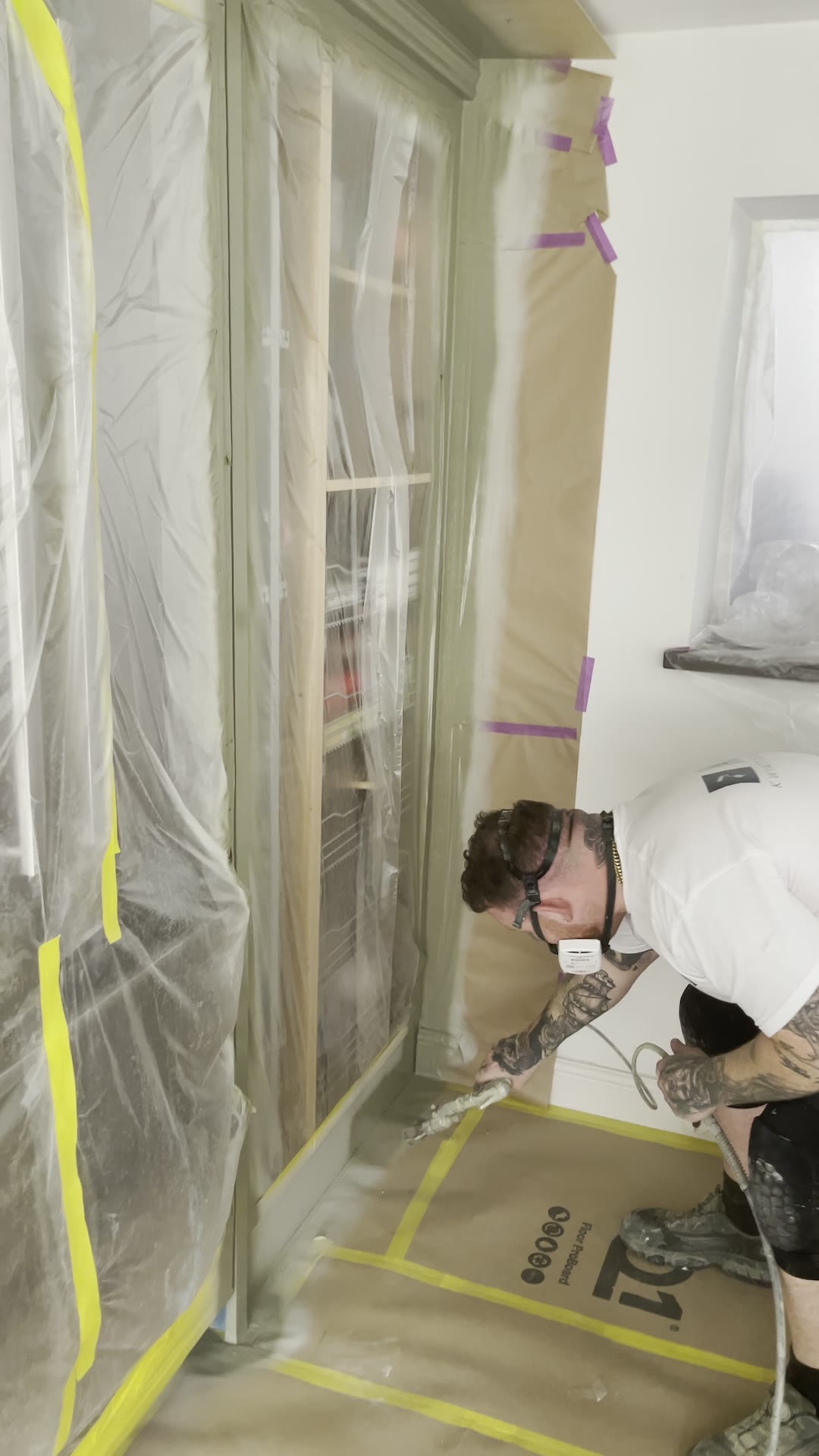 Sprayer applying a sage green Renner coating to masked kitchen larder doors in a London home